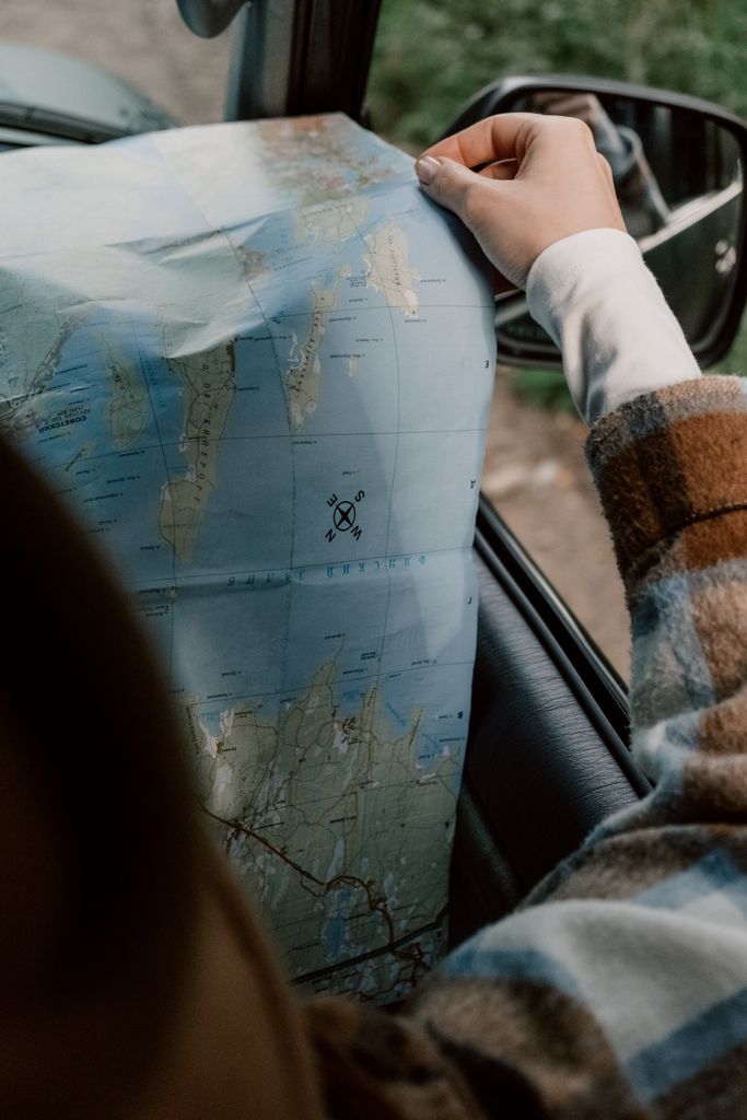 A woman in a plaid shirt holds a map while traveling in a car.